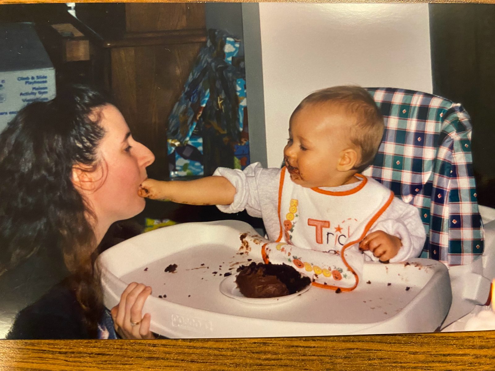 Timothy as a baby in a high chair, reaching over a tray of chocolate cake to feed a fistful of it to his mom.